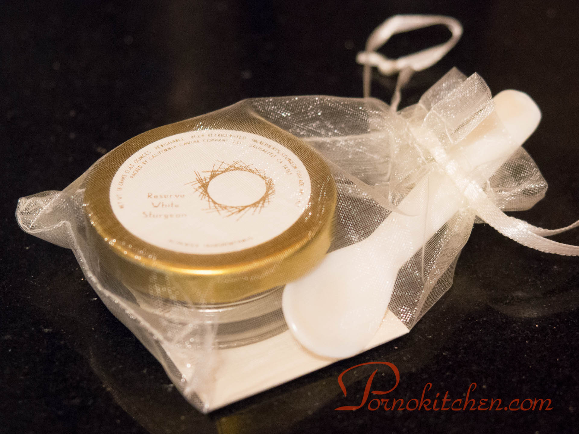 A jar of caviar with a smooth polished bone spoon in a fine mesh bag, tied with a satin ribbon.
